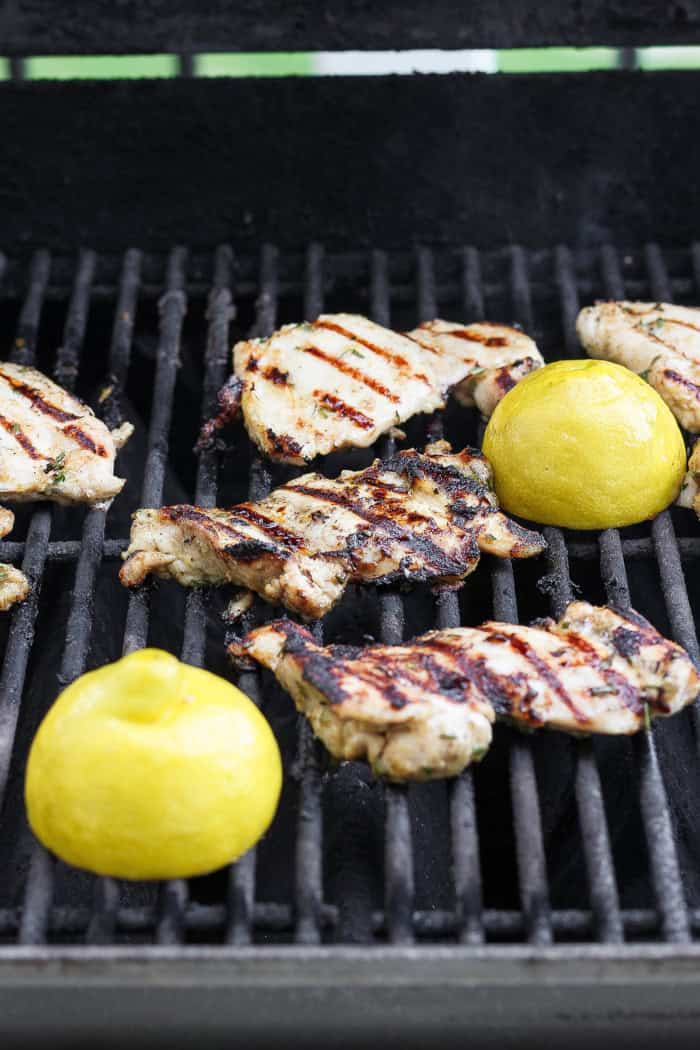 Chicken thighs and lemon halves on grill.
