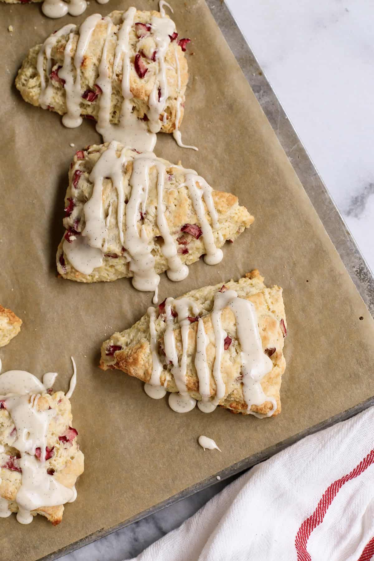 overhead photo of baked rhubarb scones with glaze, on a baking sheet with parchment paper