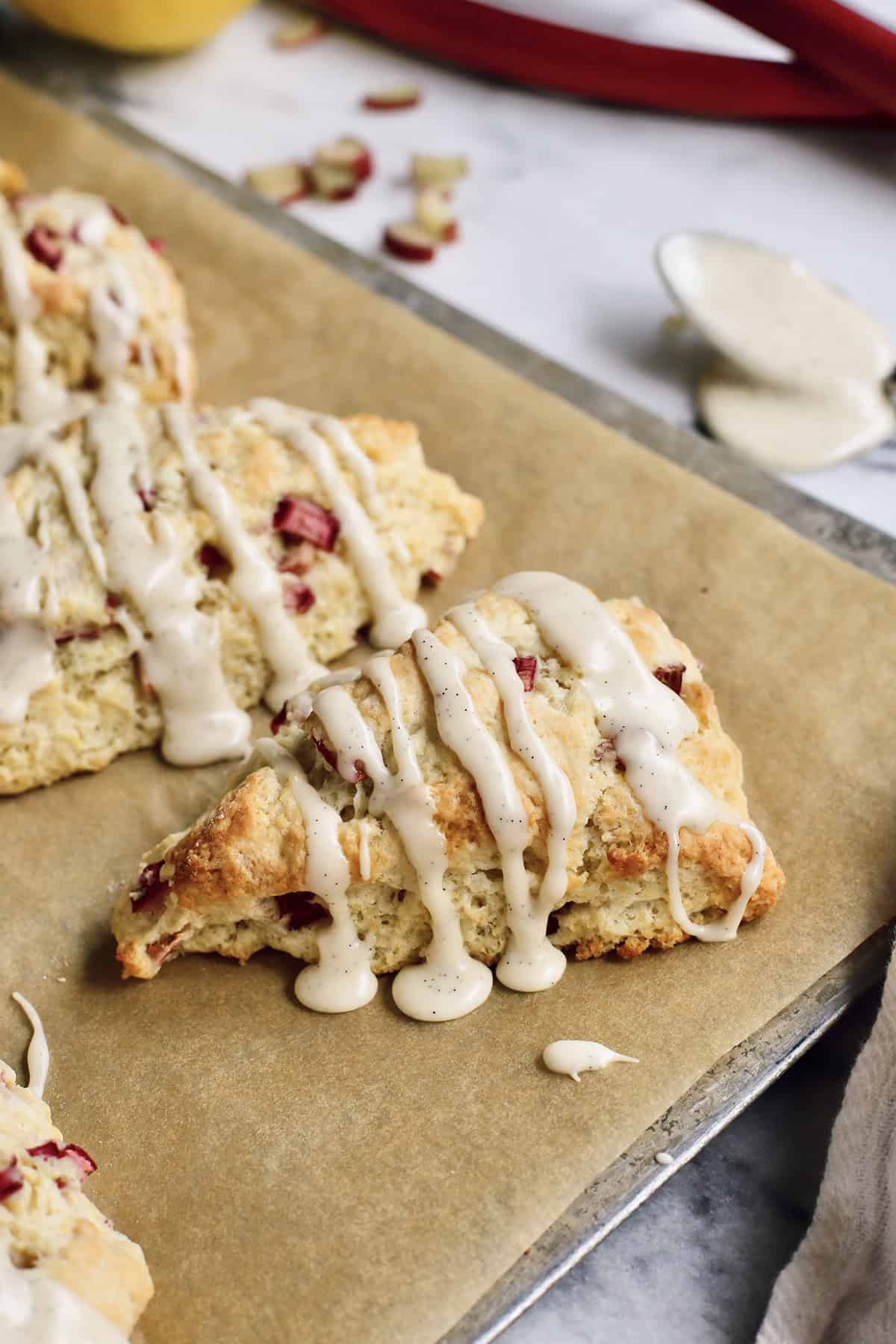 baked rhubarb scones with glaze, on a baking sheet with parchment paper