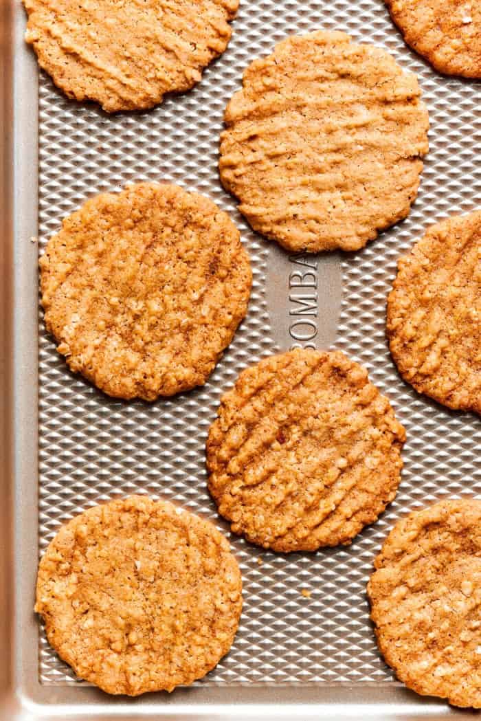 Crispy oat cookies on textured baking sheet.