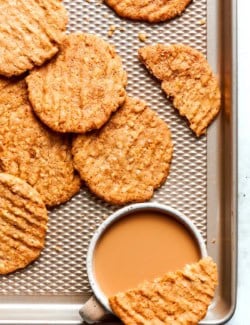 Crispy oat cookies on sheet pan with cup of coffee.