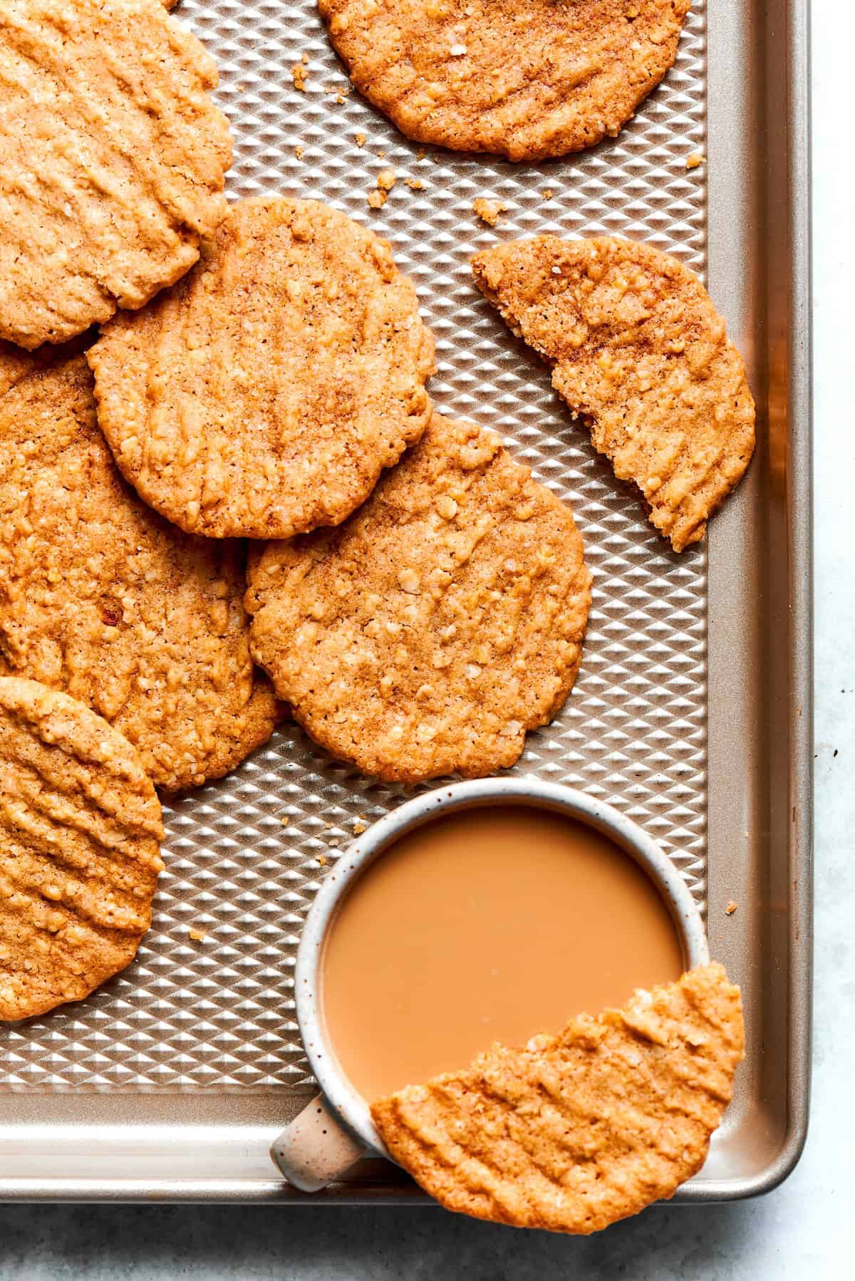 Crispy oat cookies on sheet pan with cup of coffee.