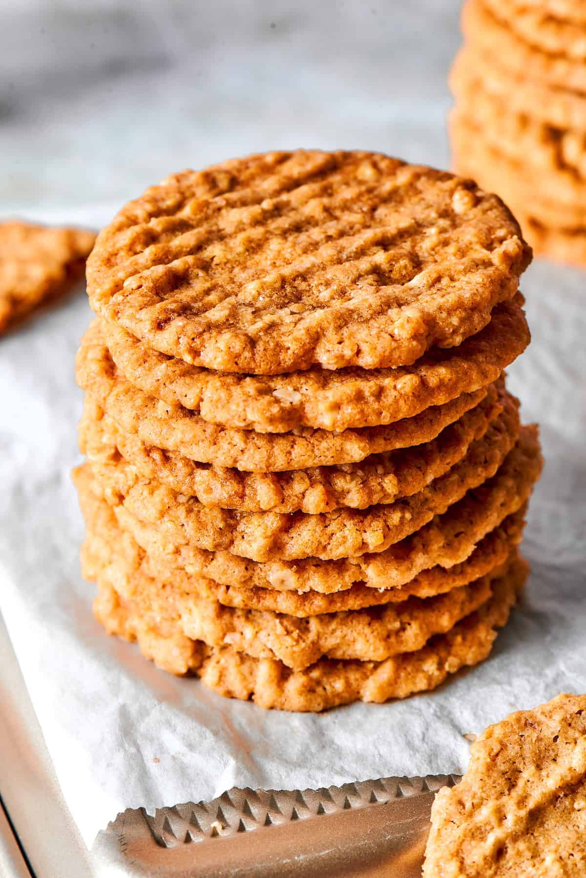 Stack of crispy oat cookies on parchment paper lined pan.