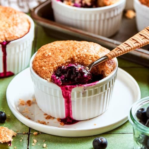 mini blueberry cobbler in a ramekin, with a spoon digging into the blueberry filling