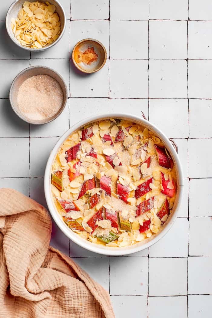 This simple Norwegian rhubarb cake is tender and delicate, with jammy rhubarb and a sprinkling of sliced almonds and cinnamon sugar on top. Unbaked Norwegian rhubarb cake in pan.
