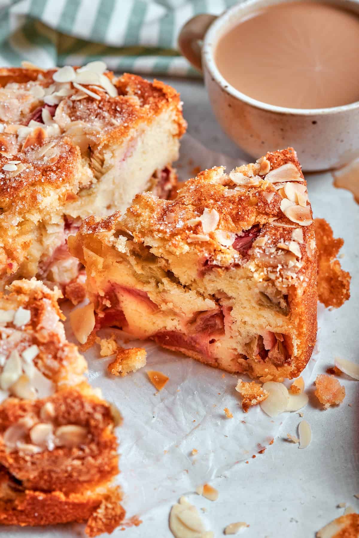 This simple Norwegian rhubarb cake is tender and delicate, with jammy rhubarb and a sprinkling of sliced almonds and cinnamon sugar on top. Slice of Norwegian rhubarb cake with cup of coffee.