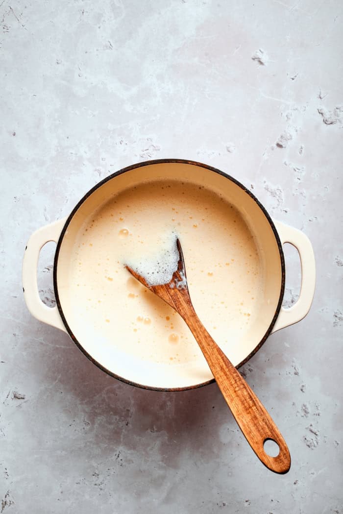This homemade rhubarb ice cream is ultra creamy, with tart rhubarb flavor and a lovely blush-pink color. Such a fun summer dessert! Custard in pot with wooden spoon.