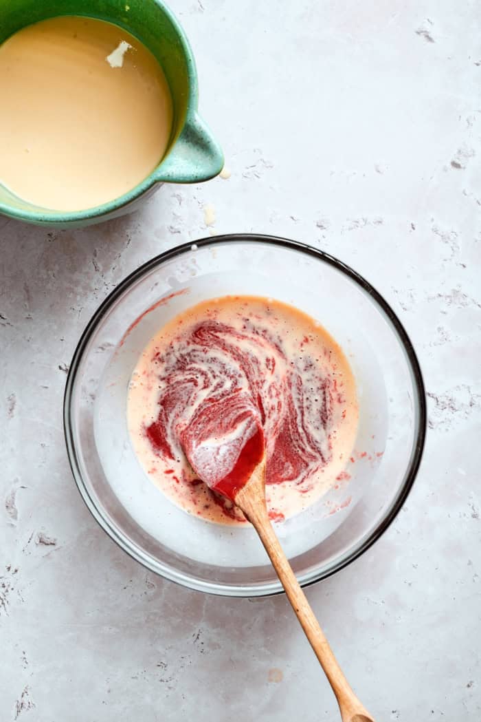 This homemade rhubarb ice cream is ultra creamy, with tart rhubarb flavor and a lovely blush-pink color. Such a fun summer dessert! Stirring rhubarb mixture and custard in bowl.