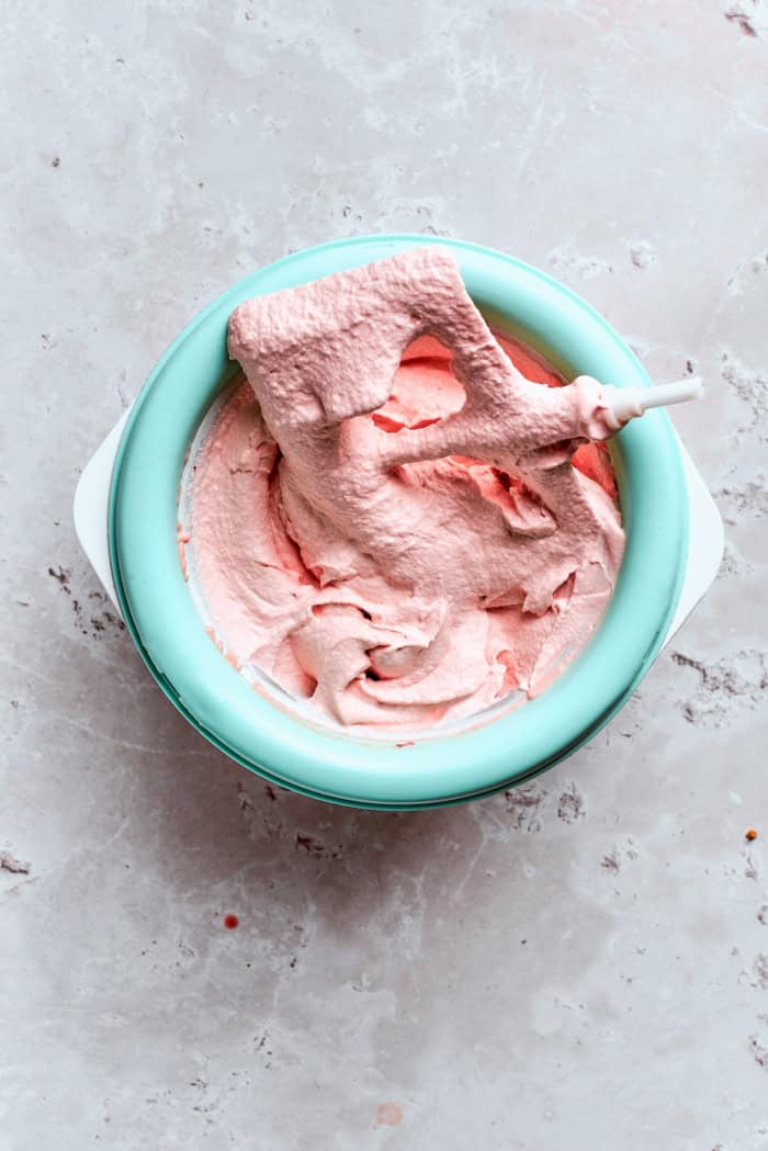This homemade rhubarb ice cream is ultra creamy, with tart rhubarb flavor and a lovely blush-pink color. Such a fun summer dessert! Rhubarb ice cream in ice cream machine.