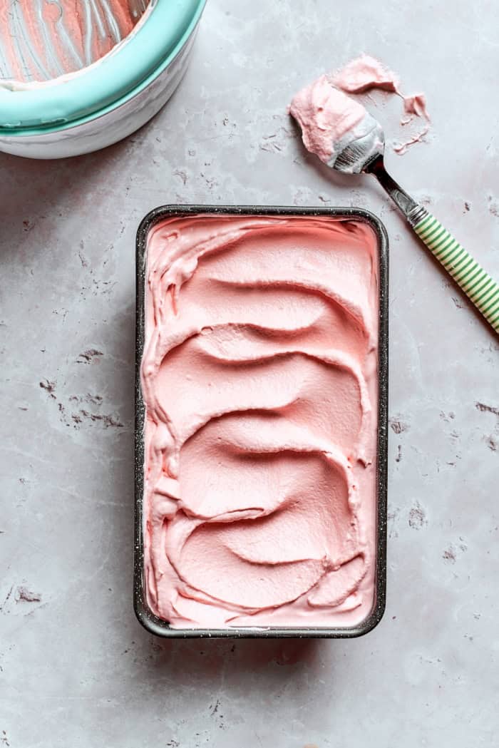This homemade rhubarb ice cream is ultra creamy, with tart rhubarb flavor and a lovely blush-pink color. Such a fun summer dessert! Loaf pan with rhubarb ice cream inside.