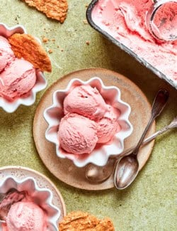 scoops of pink rhubarb ice cream in white fluted bowls, with crispy oat cookies