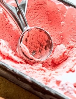 Ice cream scoop in loaf pan of rhubarb ice cream.