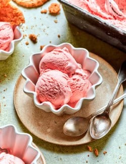 scoops of pink rhubarb ice cream in white fluted bowls, with crispy oat cookies