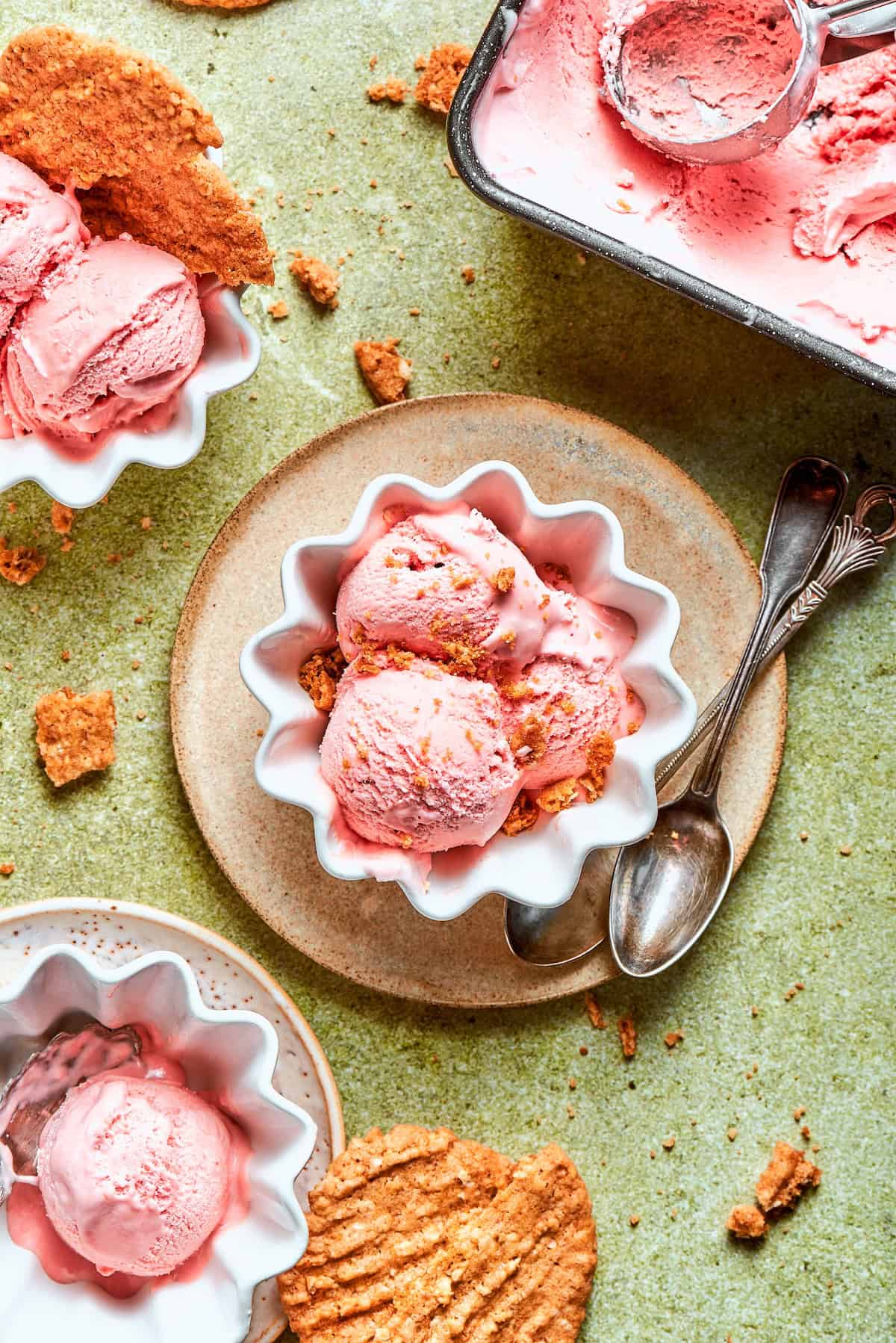 This homemade rhubarb ice cream is ultra creamy, with tart rhubarb flavor and a lovely blush-pink color. Such a fun summer dessert! Bowls of rhubarb ice cream with oat cookie crumbs.