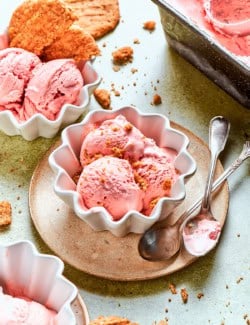 scoops of pink rhubarb ice cream in white fluted bowls, with crispy oat cookies