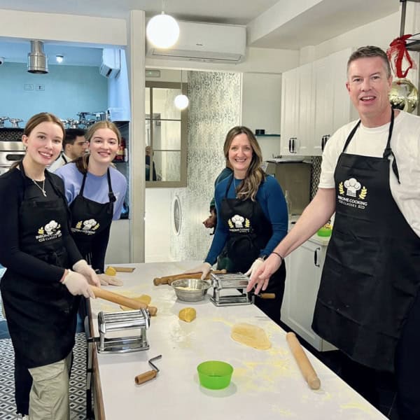 a family of four wearing black aprons, making fresh pasta at a cooking school in Rome, Italy