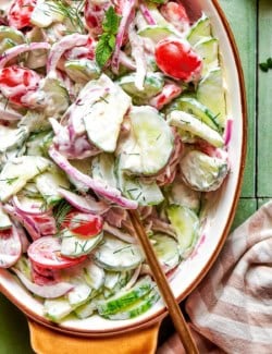 close-up overhead photo of a creamy salad of fresh cucumbers and tomatoes in an oval serving bowl