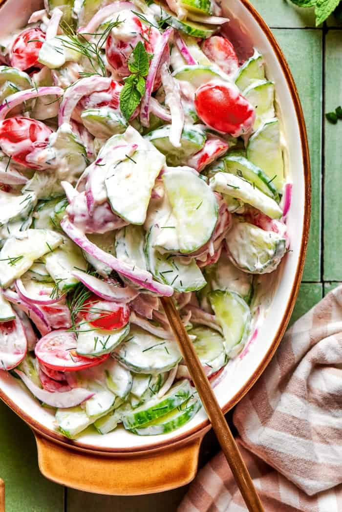 With fresh vegetables and a creamy herbed dressing, this cucumber and tomato salad is the perfect goes-with-anything side dish for summer. close-up overhead photo of a creamy salad of fresh cucumbers and tomatoes in an oval serving bowl