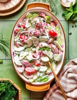 overhead photo of a creamy salad of fresh cucumbers and tomatoes in an oval serving bowl