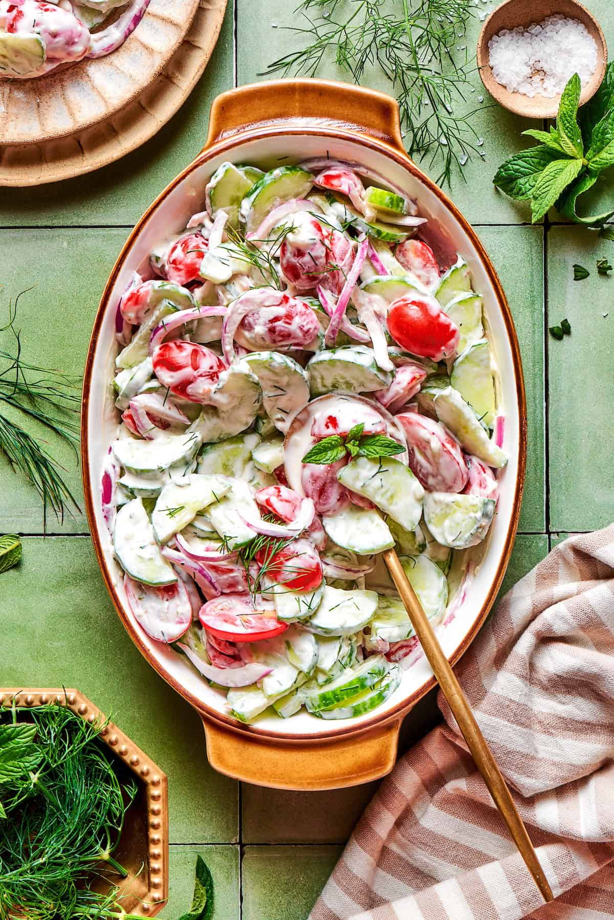 With fresh vegetables and a creamy herbed dressing, this cucumber and tomato salad is the perfect goes-with-anything side dish for summer. overhead photo of a creamy cucumber and tomato salad in an oval serving bowl
