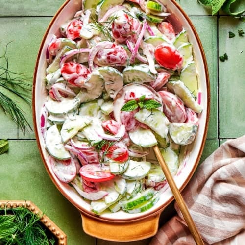 overhead photo of a creamy salad of fresh cucumbers and tomatoes in an oval serving bowl