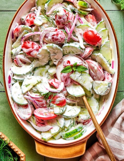 overhead photo of a creamy salad of fresh cucumbers and tomatoes in an oval serving bowl