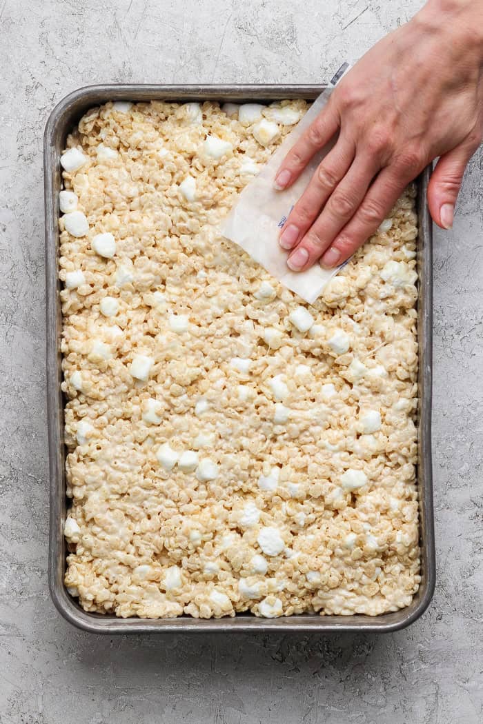 Brown butter Rice Krispie treats are a more indulgent version of the classic, with extra marshmallows, nutty brown butter and flaky sea salt! Hand pressing brown butter rice krispie treat mixture in pan with butter wrapper.