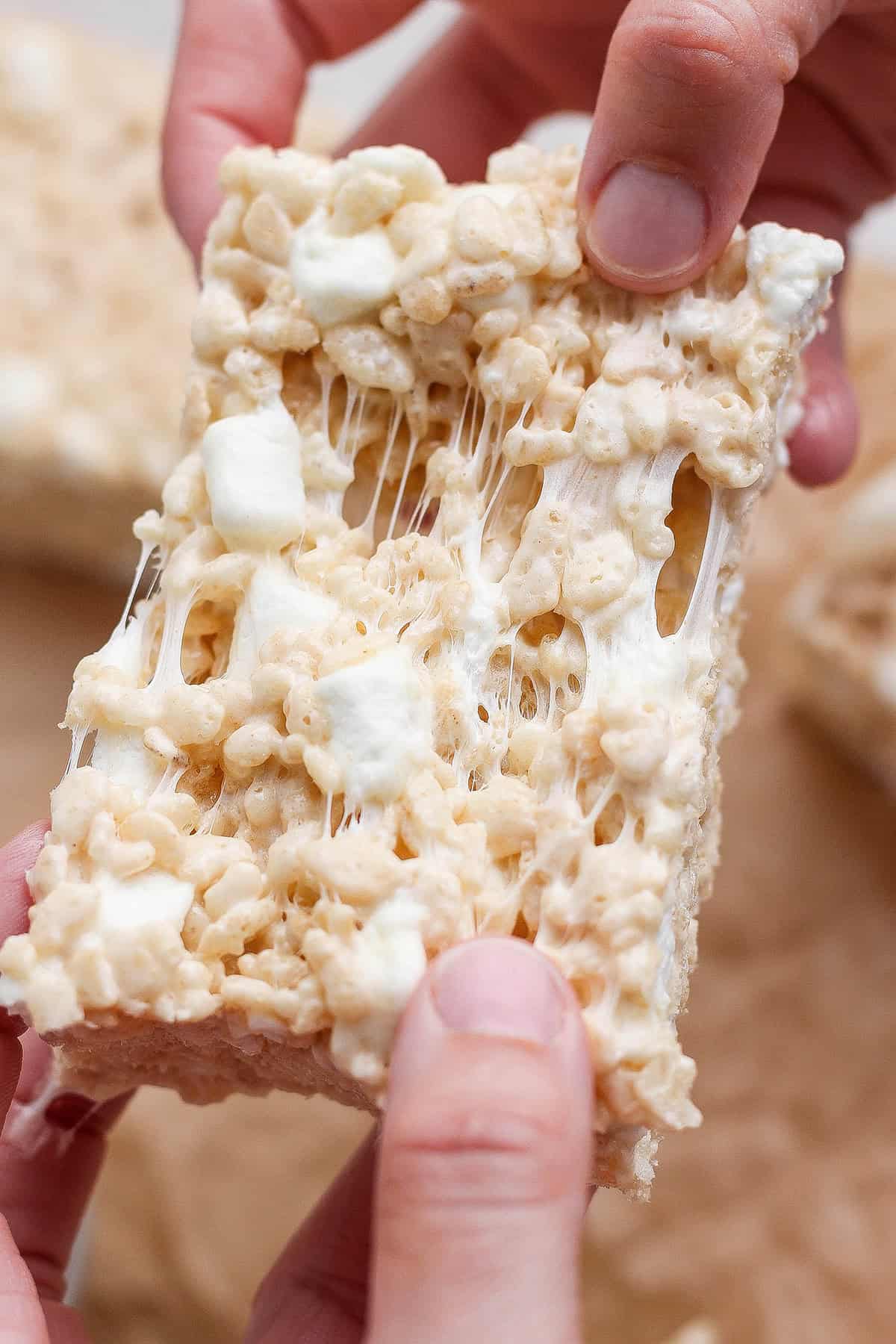 Brown butter Rice Krispie treats are a more indulgent version of the classic, with extra marshmallows, nutty brown butter and flaky sea salt! Hands pulling apart sticky brown butter rice krispie treat.