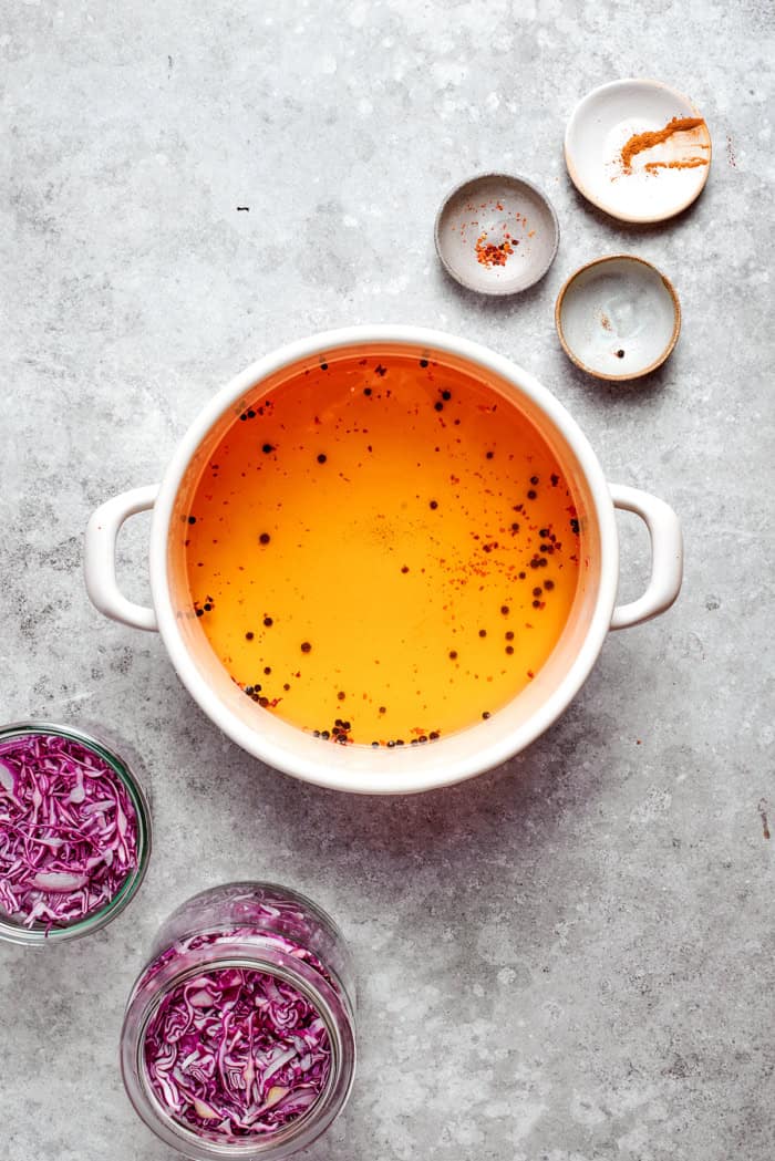 two jars with shredded red cabbage and a pot of pickling brine