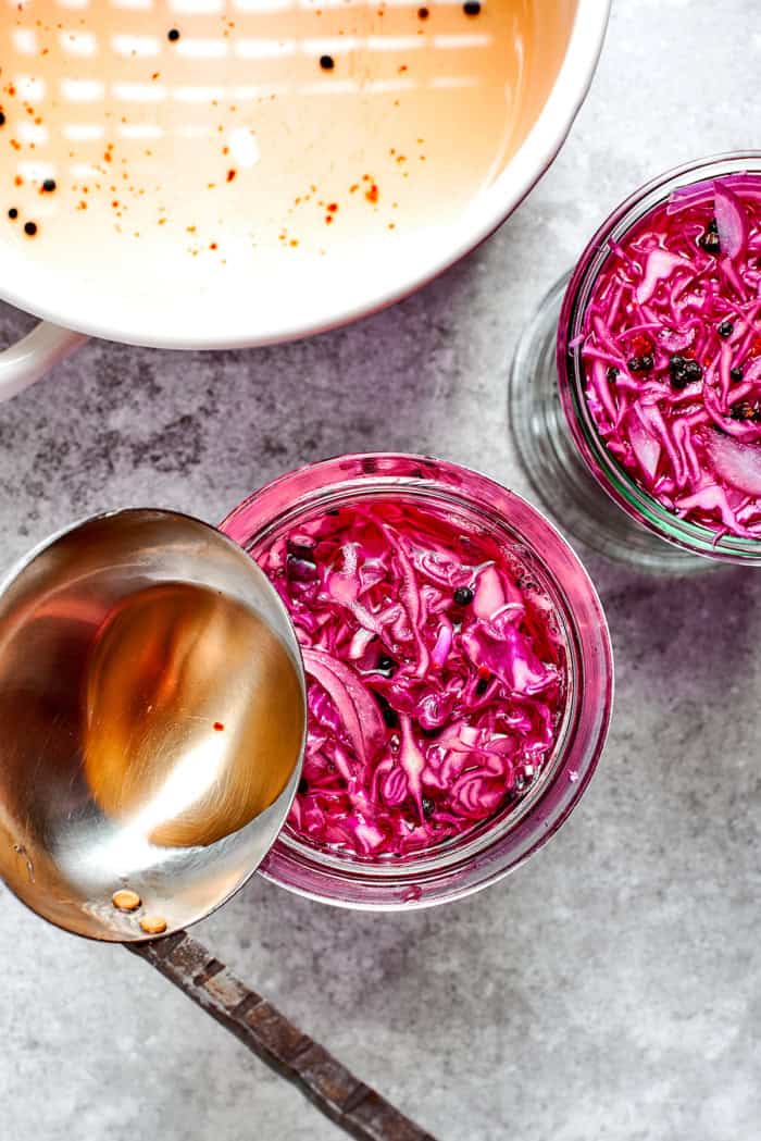 a ladle pouring pickling brine over shredded red cabbage in glass jars