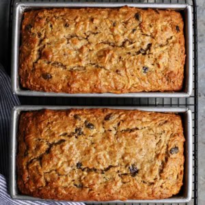 overhead photo of two baked loaves of apple bread in loaf pans, on a wire cooling rack