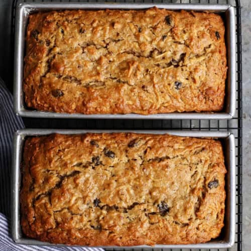 overhead photo of two baked loaves of apple bread in loaf pans, on a wire cooling rack