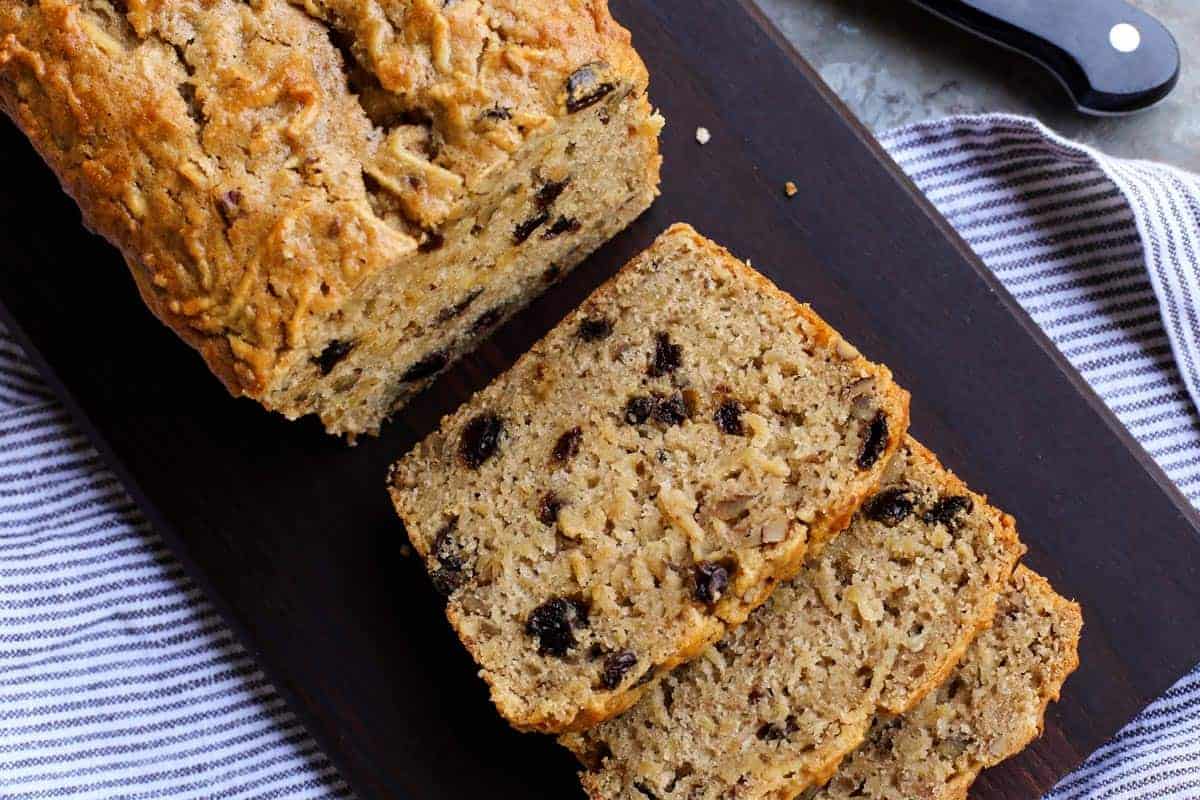 overhead photo of a loaf of apple bread with raisins, cut into slices on a cutting board