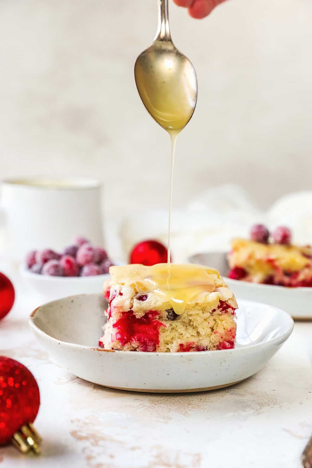 a spoonful of creamy butter sauce being drizzled over a piece of cranberry cake in a white speckled dish
