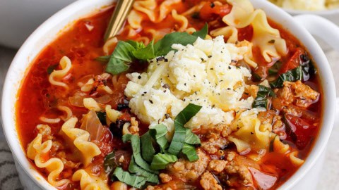 close-up photo of lasagna soup with dollop of cheesy yum and fresh basil on top, in white bowl