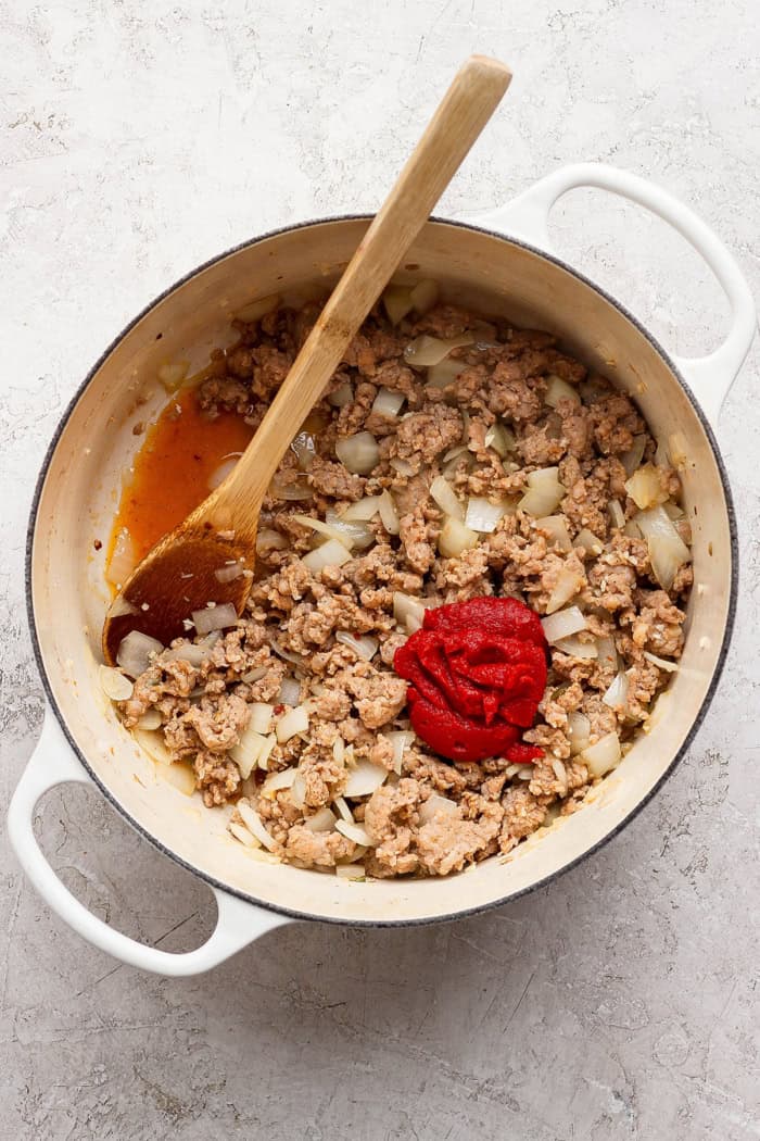 cooked sausage and onion in a large white pot, with a dollop of tomato paste
