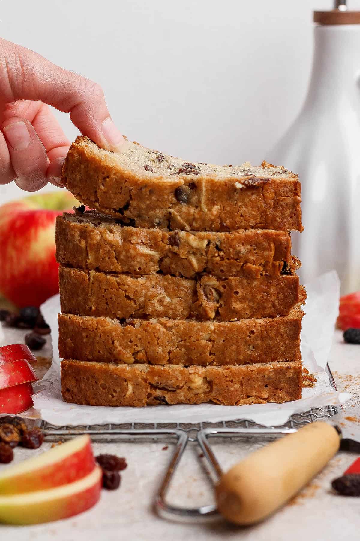 a stack of apple bread slices with a hand bending the top slice upward to show how moist it is