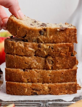 a stack of apple bread slices with a hand bending the top slice upward to show how moist it is