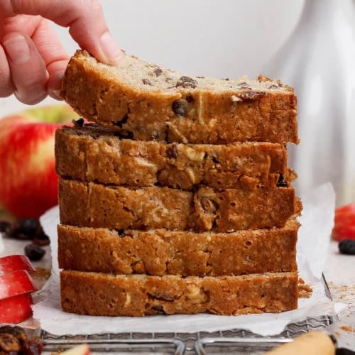 a stack of apple bread slices with a hand bending the top slice upward to show how moist it is