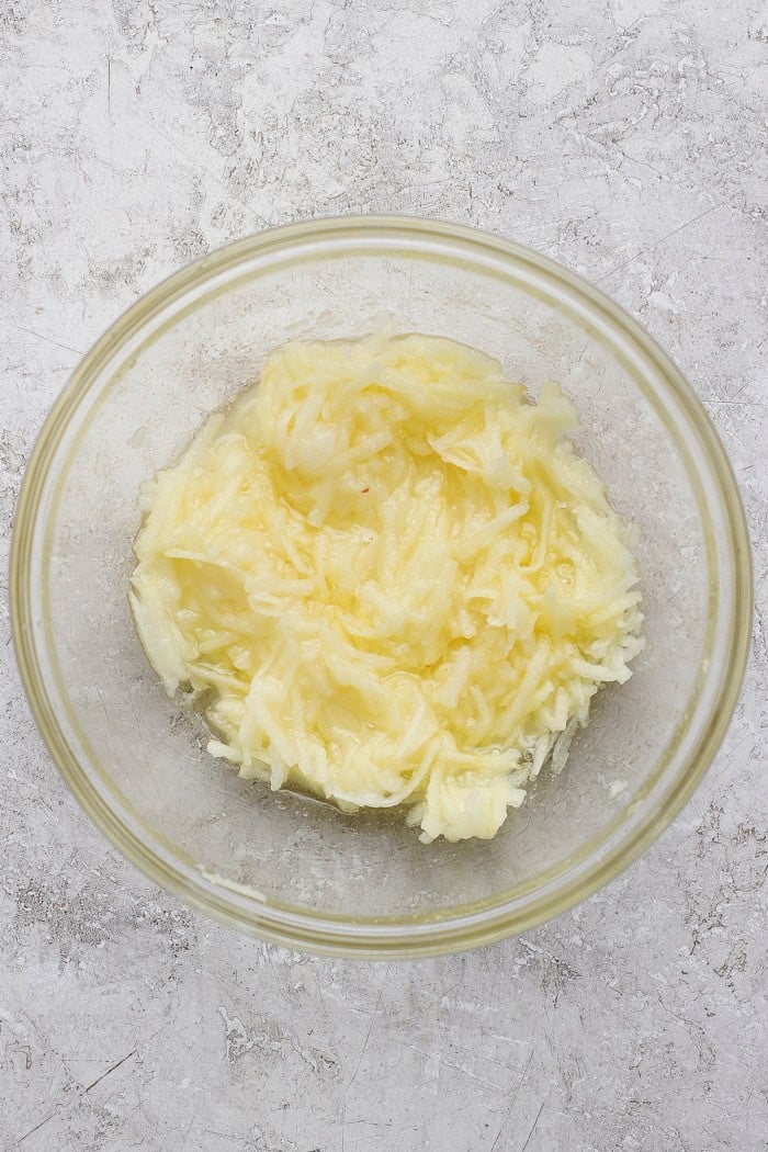a clear mixing bowl with shredded apples