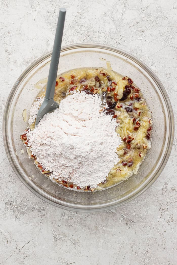 a clear mixing bowl with wet shredded apple mixture and dry ingredients, before they are mixed together