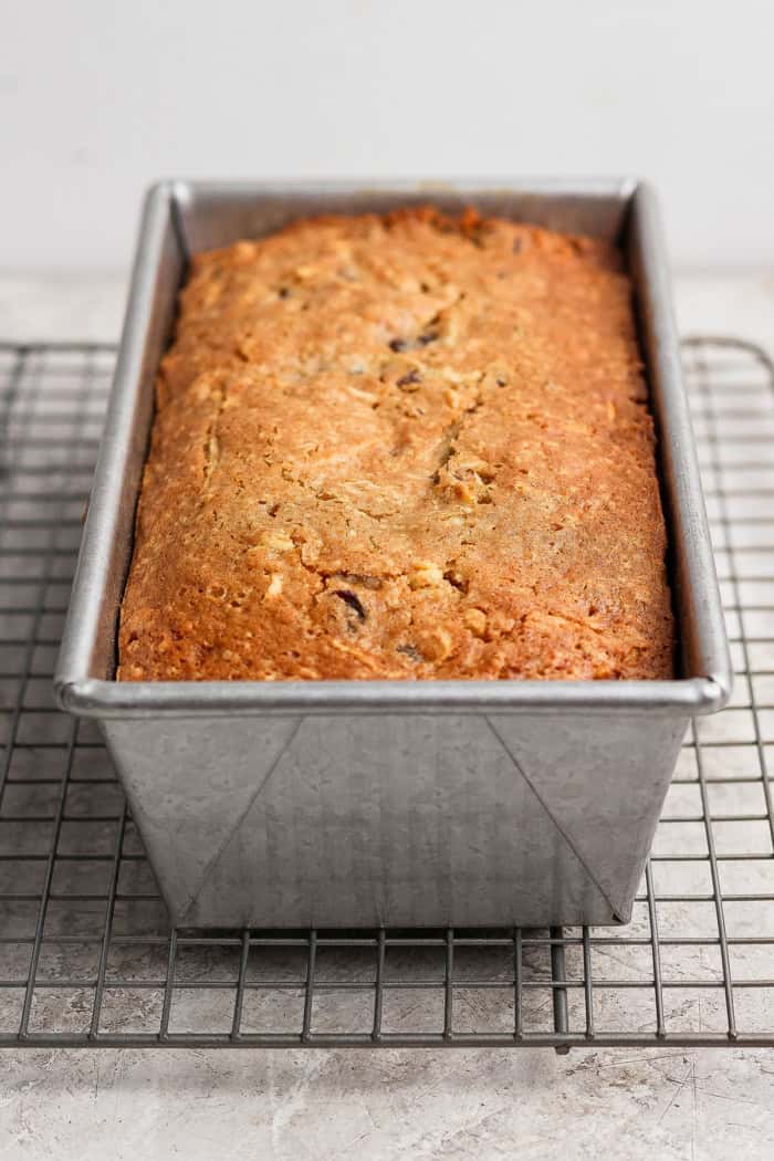 baked apple bread in a loaf pan on a wire cooling rack